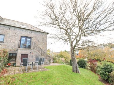 A stone house with outdoor stairs and patio furniture on a grassy yard with a tree at Magnolia House in Dittisham
