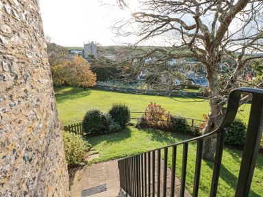 An outdoor view from stairs with a stone wall on the left a tree and bushes overlooking a grassy field and a church in the background at Magnolia House in Dittisham