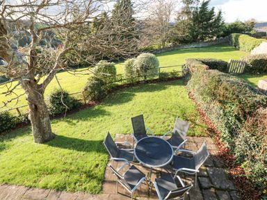 A garden with a table and six chairs on a stone patio surrounded by grass and hedges at Magnolia House in Dittisham