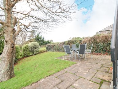 An outdoor patio with a table and four chairs next to a grassy lawn and trees at Magnolia House in Dittisham