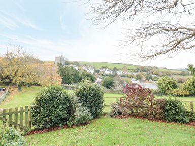 A garden with bushes and a wooden fence overlooking a village and church in the background at Magnolia House in Dittisham