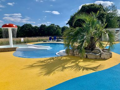 An outdoor swimming pool area with a mushroom water feature a palm tree on rocks and lounge chairs at Owls Nest in Furzehill