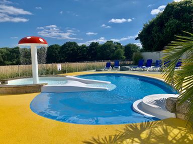 An outdoor pool area with a mushroom water feature blue lounge chairs and trees in the background at Owls Nest in Furzehill