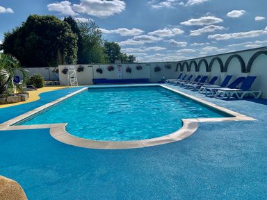 An outdoor swimming pool with blue lounge chairs and yellow and blue flooring at Owls Nest in Furzehill