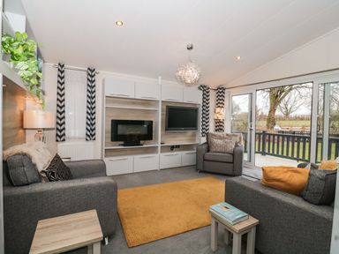 A living room with gray sofas an orange rug a wall-mounted TV and large windows opening to a garden at Owls Nest in Furzehill