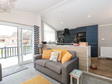 A living room with a gray sofa and yellow cushions next to a kitchen with blue cabinets at Owls Nest in Furzehill