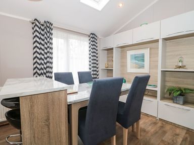 A dining area with a marble table and blue chairs near a window with patterned curtains at Owls Nest in Furzehill