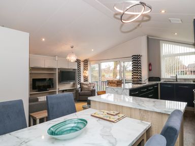 An open plan kitchen and living area with dining table blue chairs a green bowl a television armchair and sliding glass doors at Owls Nest in Furzehill
