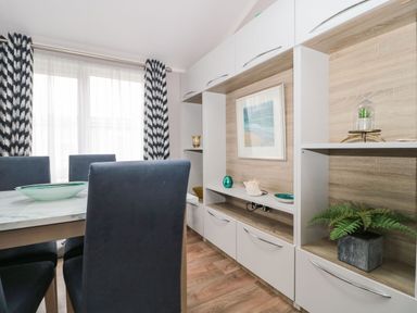 A dining area with a table and chairs next to a shelving unit with decorative items at Owls Nest in Furzehill