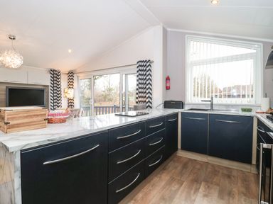 A kitchen with dark cabinets a marble countertop a window with vertical blinds and sliding glass doors at Owls Nest Furzehill