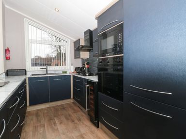 A kitchen with dark blue cabinets wooden floor and a window with vertical blinds at Owls Nest in Furzehill