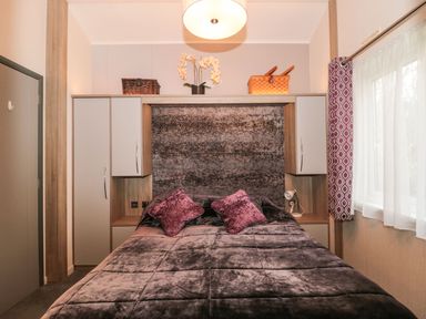 A bedroom with a bed two pillows overhead cabinets and a window with curtains at Owls Nest in Furzehill