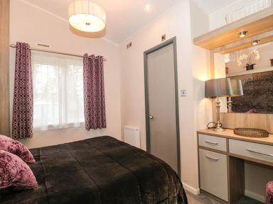 A bedroom with a bed a window with curtains a door and a vanity with a lamp at Owls Nest in Furzehill