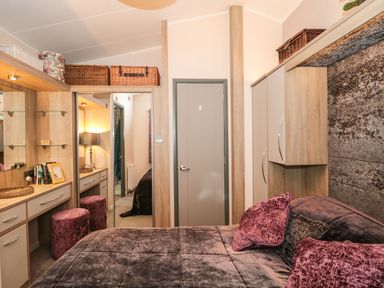 A bedroom with a bed with pillows a dressing table with two stools and a door at Owls Nest in Furzehill
