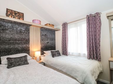 A bedroom with two single beds a lamp between them and patterned curtains at Owls Nest in Furzehill
