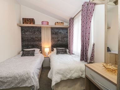 A bedroom with two single beds a bedside table with a lamp patterned curtains and a dresser at Owls Nest in Furzehill
