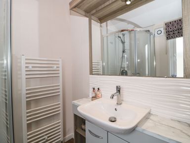 A bathroom with a white sink, a mirror, a towel radiator, and a glass shower enclosure at Owls Nest in Furzehill