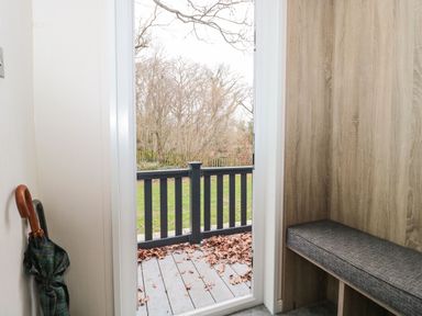 A corner with an umbrella stand and bench next to a door opening onto a deck with leaves at Owls Nest in Furzehill