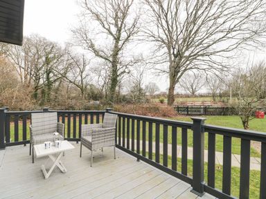 An outdoor deck with two wicker chairs and a small table with a teapot and cups overlooking a grassy area with trees at Owls Nest in Furzehill