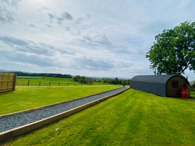 A grassy field with a gravel path and a long black curved structure under a tree at Dryfe Lodge in Lockerbie