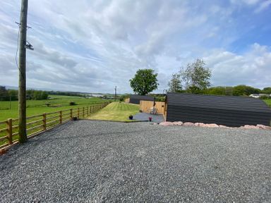 A gravel area with two pod-shaped buildings on a grassy field surrounded by wooden fences at Dryfe Lodge in Lockerbie