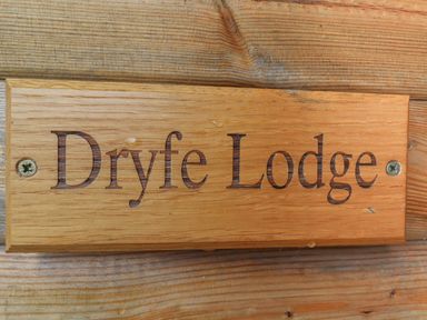 A wooden sign with the text Dryfe Lodge mounted on a wooden surface at Dryfe Lodge in Lockerbie
