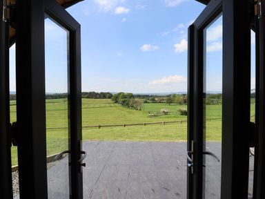 A view of green fields and trees through open glass doors at Dryfe Lodge in Lockerbie