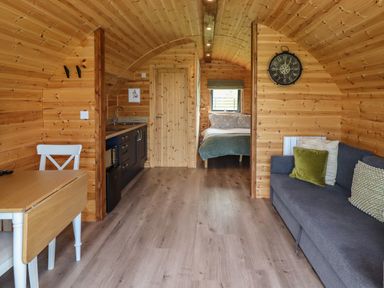 An interior view of a wooden cabin with a kitchen area dining table sofa and a bedroom visible at Dryfe Lodge in Lockerbie