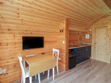A small wooden kitchen area with a foldable table and two chairs next to a mounted TV at Dryfe Lodge in Lockerbie
