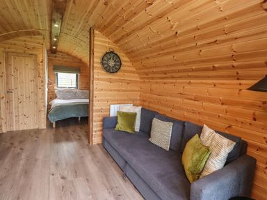 A wooden interior living space with a gray sofa with cushions and a bedroom with a bed in the background at Dryfe Lodge in Lockerbie