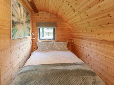 A wooden bedroom with a bed under a small window and a wall picture at Dryfe Lodge in Lockerbie