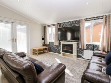 A living room with two brown leather sofas a wall mounted television and a fireplace at Lake View Lodge Lakeside 3 White Cross Bay Windermere