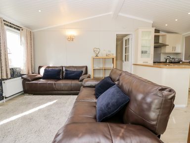 A living room with two brown leather sofas and a white rug near an open kitchen at Lake View Lodge in Lakeside 3 White Cross Bay Windermere
