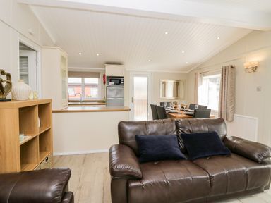 A living room with a brown leather sofa and a wooden shelf next to an open kitchen and dining area at Lake View Lodge Lakeside 3 White Cross Bay Windermere