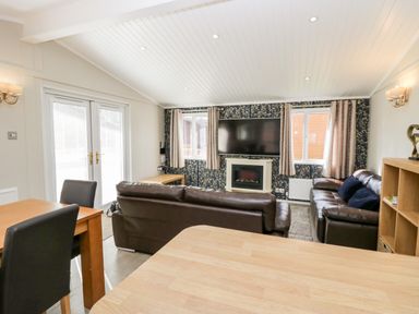 A living room with leather sofas a wall mounted television a fireplace a dining table with chairs and glass doors at Lake View Lodge in Lakeside 3 White Cross Bay Windermere
