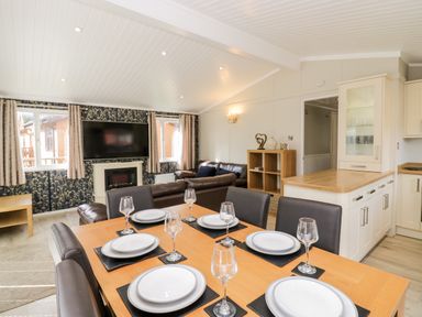 A dining area with a wooden table set for six people and a living room with a sofa and wall-mounted TV at Lake View Lodge in Lakeside 3 White Cross Bay Windermere