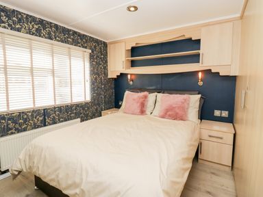 A bedroom with a double bed covered with white bedding and pink pillows two bedside tables wooden built in cupboards and a window with blinds at Lake View Lodge in Lakeside 3 White Cross Bay Windermere