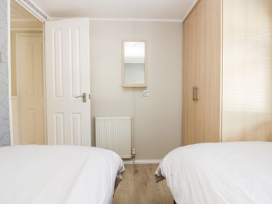 A bedroom with two beds a wooden wardrobe a white door a radiator and a mirror on the wall at Lake View Lodge Lakeside 3 White Cross Bay Windermere