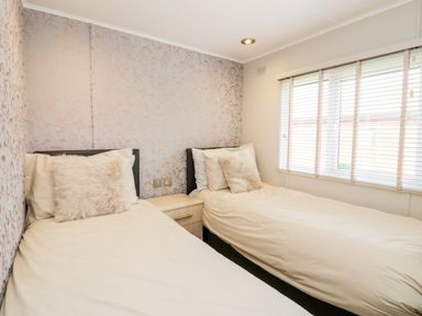 A bedroom with two single beds separated by a small nightstand with a window with blinds on the right at Lake View Lodge in Lakeside 3 White Cross Bay Windermere