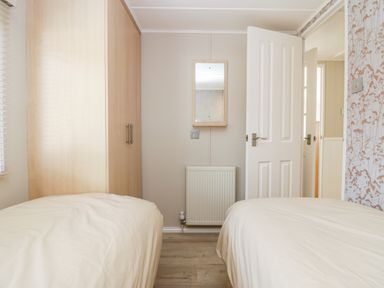 A bedroom with two beds a wooden wardrobe a wall mirror and a radiator at Lake View Lodge in Lakeside 3 White Cross Bay Windermere