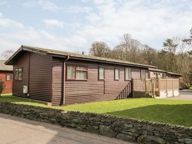 An exterior view of a single-story wooden lodge with a small deck and a stone wall in front at Lake View Lodge in Lakeside 3 White Cross Bay Windermere