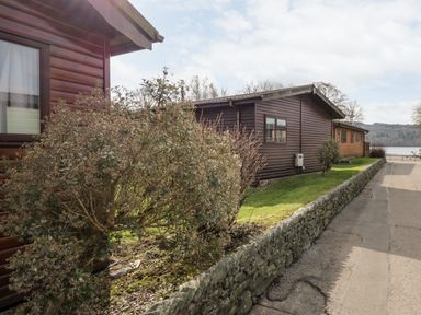 A pathway beside wooden lodges with bushes and a stone wall at Lake View Lodge in Lakeside 3 White Cross Bay Windermere