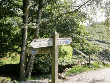 A wooden signpost with direction signs for Grasmere and Ambleside on a dirt path with trees and greenery around at Lake View Lodge in Lakeside 3 White Cross Bay Windermere