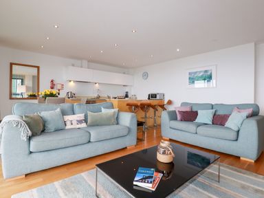 A living room with two sofas a black coffee table and a kitchen area with bar stools at Fistral Pearl in Newquay