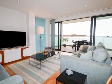A living room with sofas coffee table and television near sliding doors leading to a balcony at Fistral Pearl in Newquay
