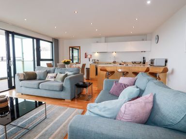 A living room with two sofas and a kitchen with bar stools at Fistral Pearl in Newquay