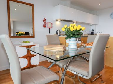 A dining area with a glass table and four beige chairs with yellow flowers in a vase on the table at Fistral Pearl in Newquay