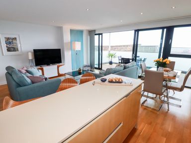 A living room with sofas and a television near a dining table and kitchen island at Fistral Pearl in Newquay