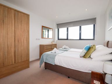 A bedroom with two single beds a wooden wardrobe a dresser with a mirror and a window with a blind at Fistral Pearl in Newquay