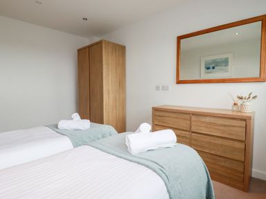 A bedroom with two single beds a wooden wardrobe a wooden dresser and a large mirror at Fistral Pearl in Newquay